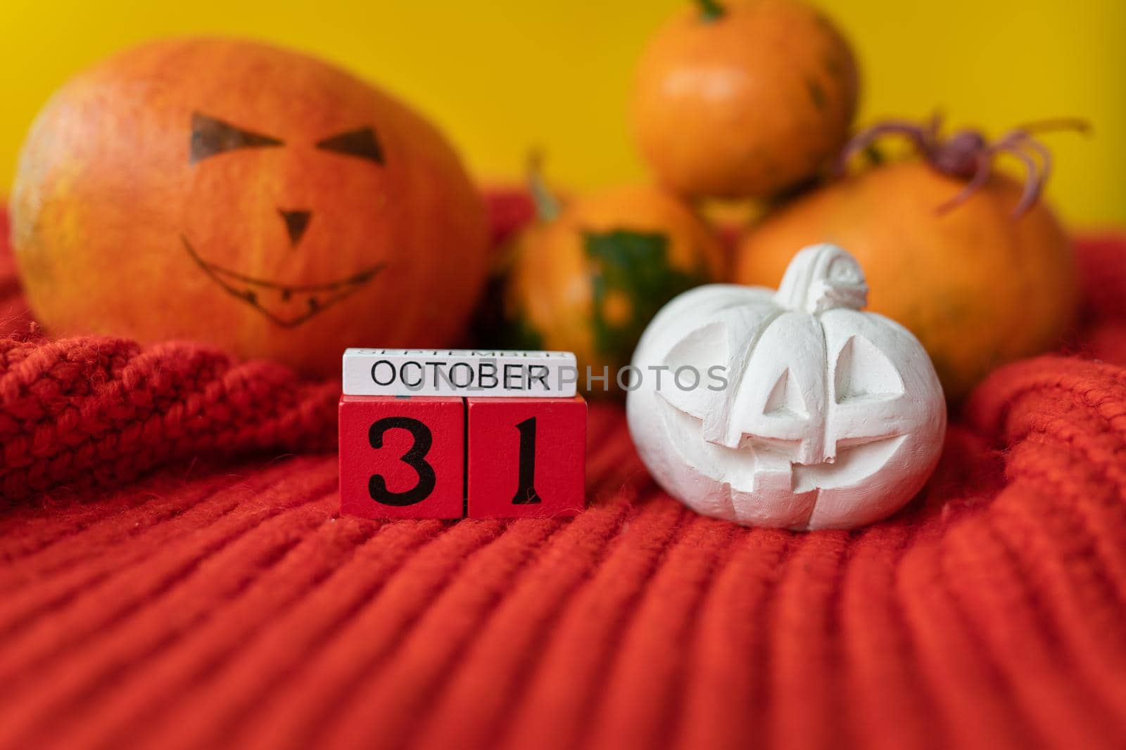 Against the background of a pumpkin with a painted face, a spider, a plaster figure, a wooden calendar on a red sweater. Holiday concept of October 31, Halloween