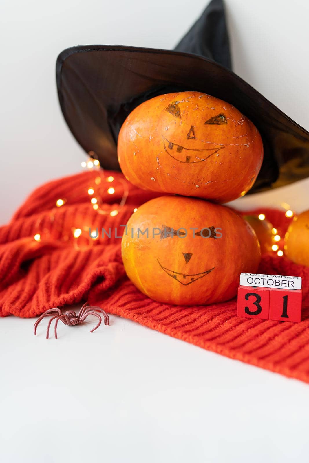 Two pumpkins with a painted face in a hat, a spider, a wooden calendar on a red sweater. Holiday concept of October 31, Halloween. Beautiful bokeh on the background