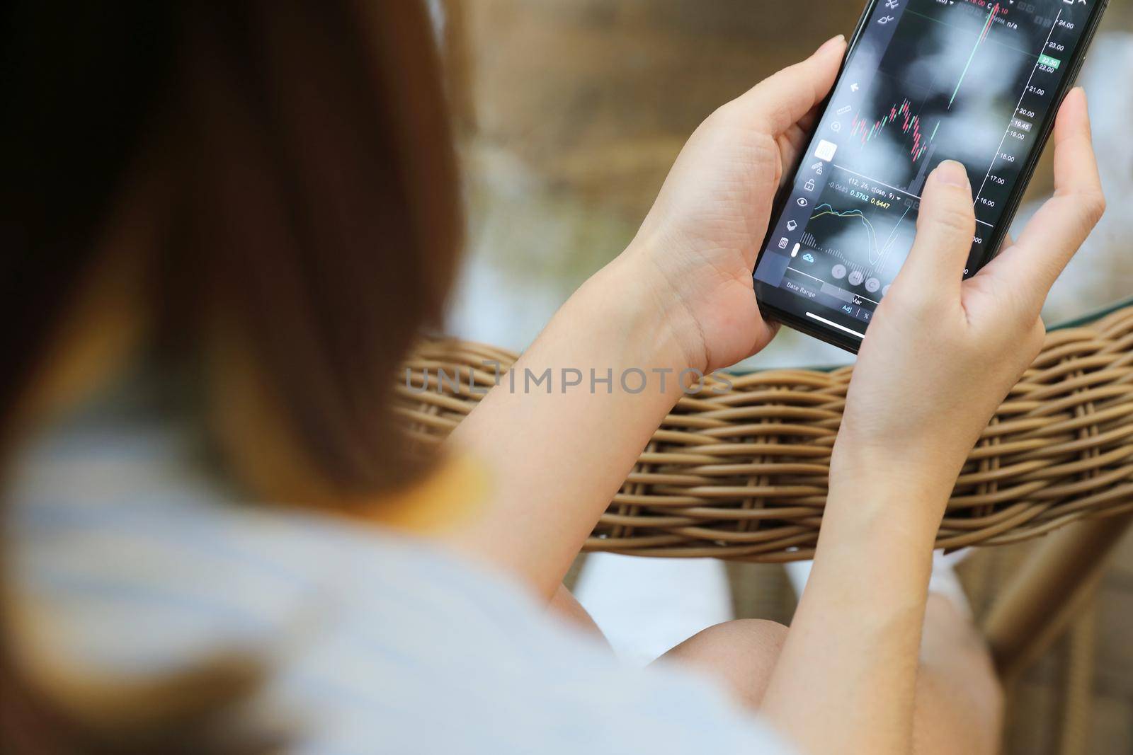 Female hand with smartphone trading stock online in coffee shop , Business concept by piyato