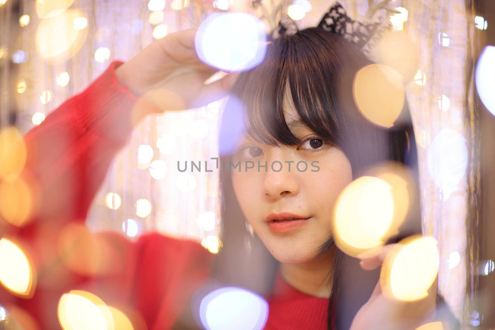 Beautiful Asian young woman with a red sweater with Christmas tree light by piyato