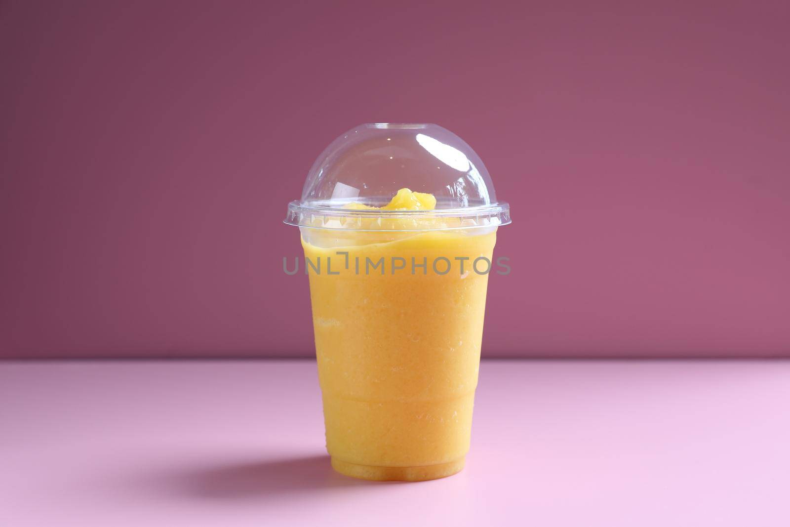 Mango smoothie milk shake with take out glass isolated on pink background by piyato