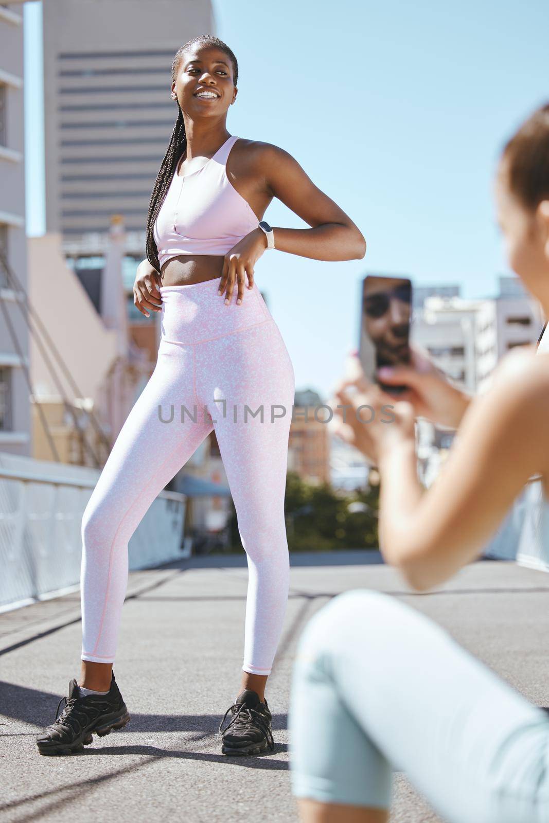 Fitness influencer friends with smartphone photo for social media update on wellness lifestyle and body progress results. Gen z marketing girl taking photo of black woman for sports fashion website.
