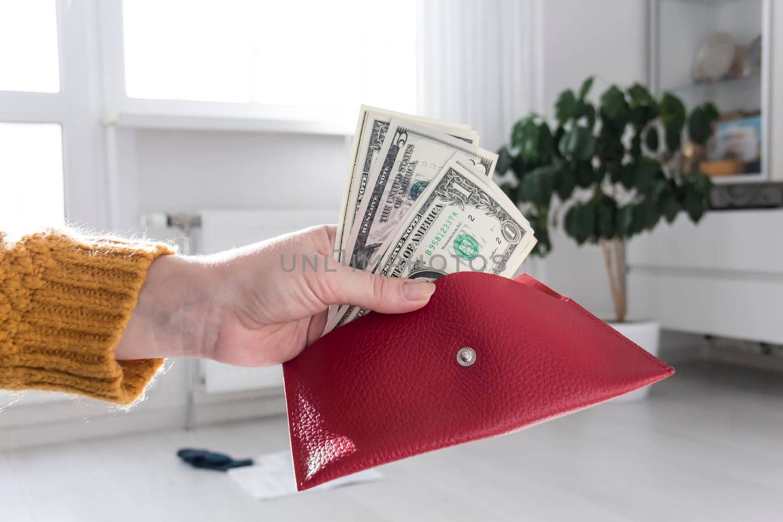 Women's hands in a yellow sweater are holding an open, red purse with money..