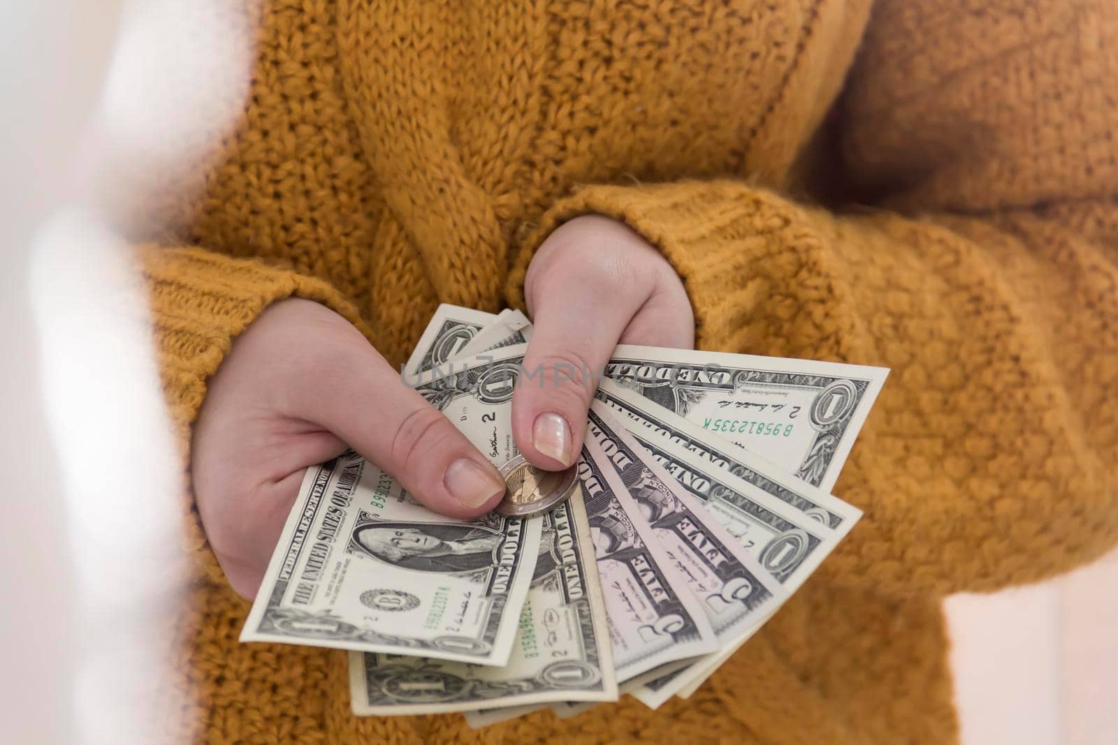 Women's hands in a yellow sweater hold small dollar bills..