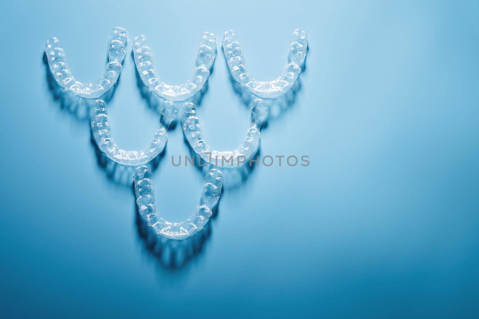 invisible plastic braces lie in a pyramid shape in a row on a blue background, studio shot, nobody by yanik88