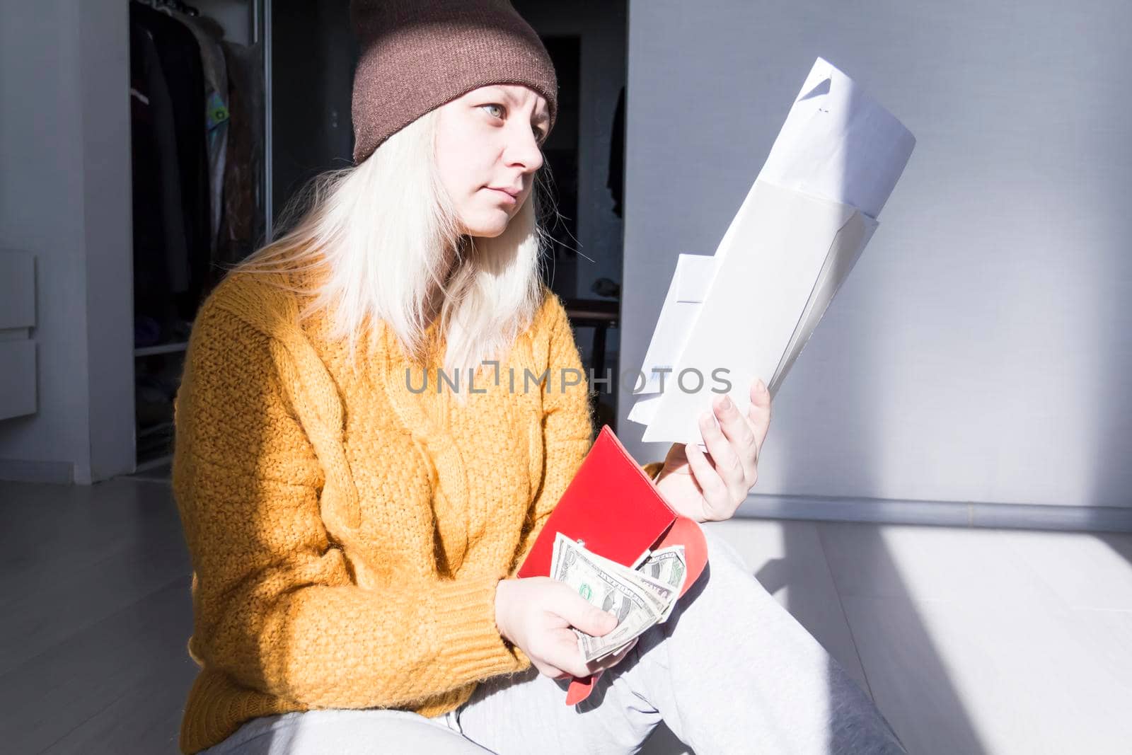 A young girl in a yellow sweater and hat is studying large bills, taxes and utility bills..