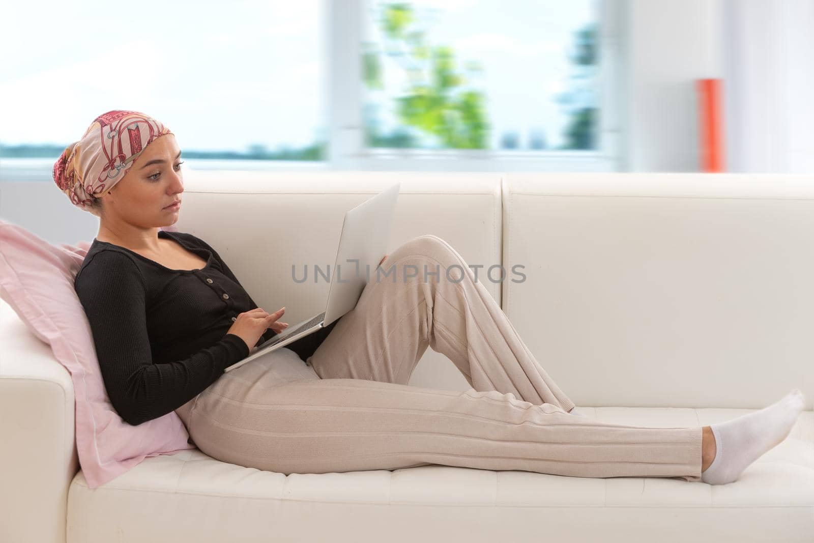 Woman a scarf in the cheuveux lying on the sofa, a laptop on her lap.