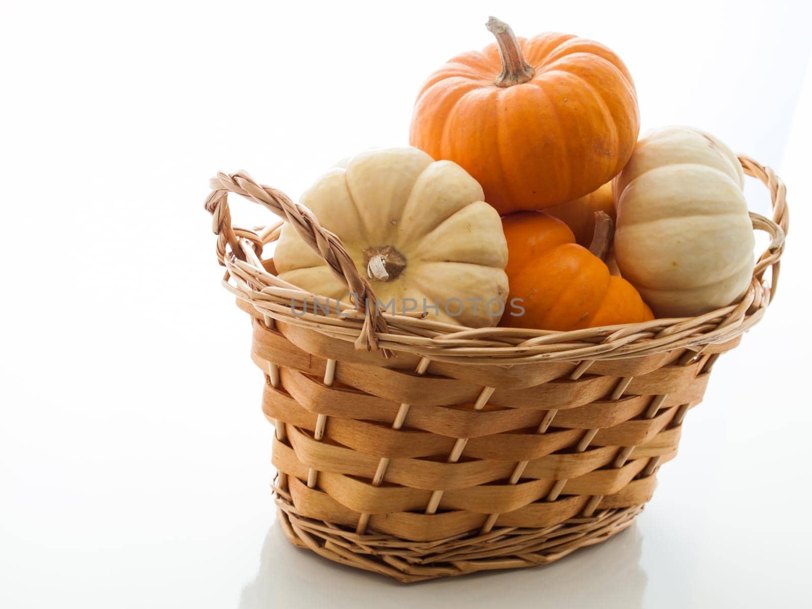 Small orange and white pumpkins in basket on white background.
