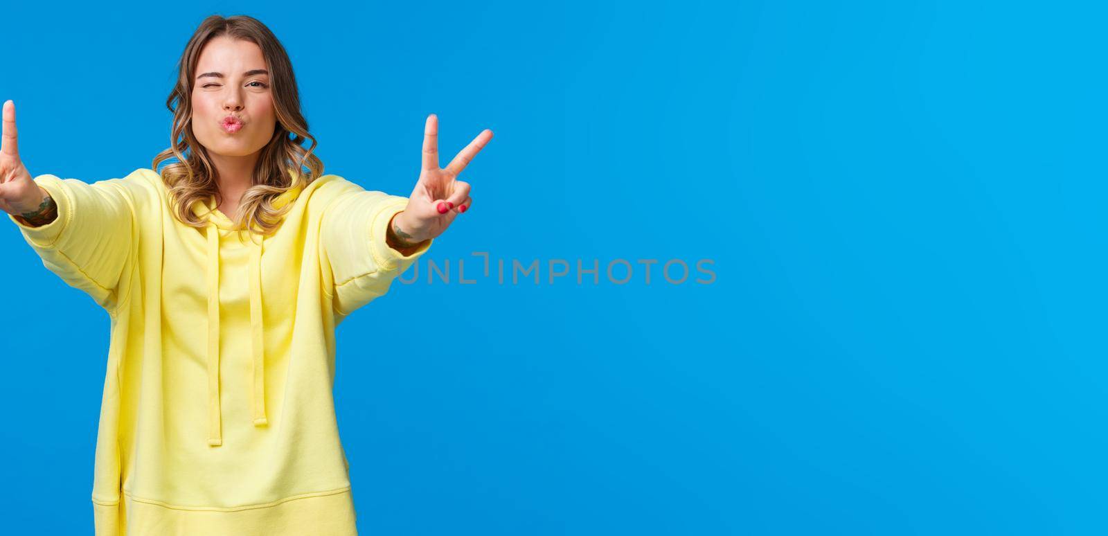 Lovely silly good-looking teenage girl send positive vibe, show peace gestures wink and make air kiss, mwah with folded lips, having fun, enjoy cool party, standing blue background by Benzoix