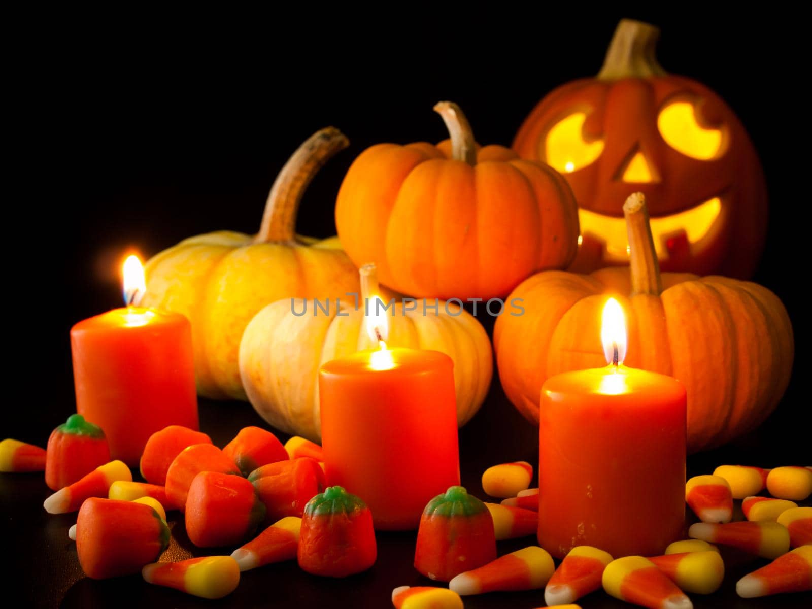 Lit orange candles with small pumpkins and jack-o'-lantern on black background.