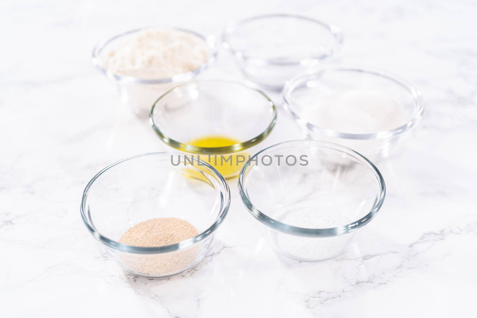 Measured ingredients in a glass mixing bowl to prepare pizza dough.