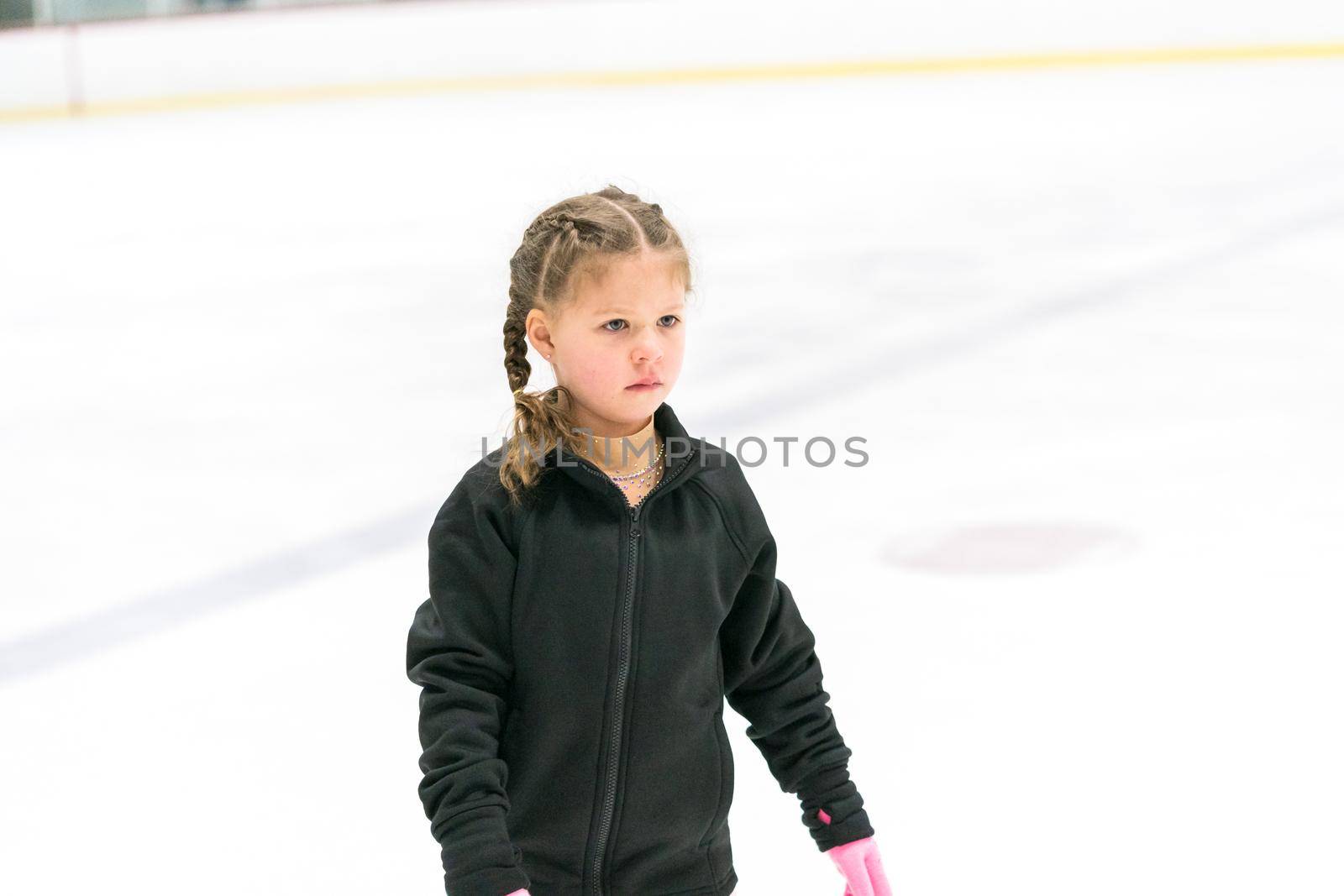 Little girl practicing figure skating on an indoor ice skating rink.