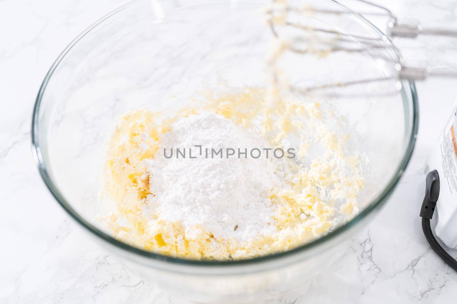 Mixing ingredients in a large glass mixing bowl to prepare cream cheese drizzle sauce.