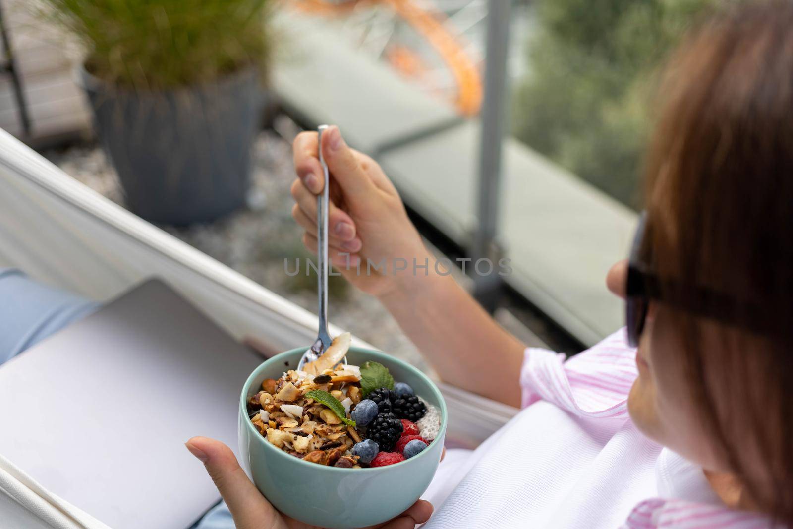 young woman eating chia pudding with nuts and berries by Chechotkin