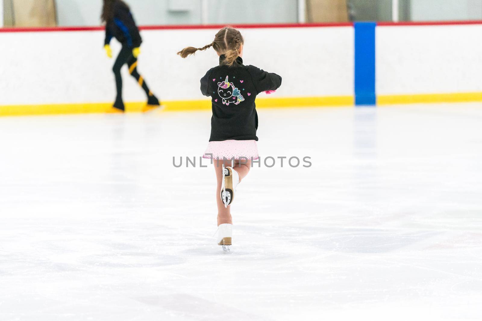 Little girl practicing figure skating on an indoor ice skating rink.