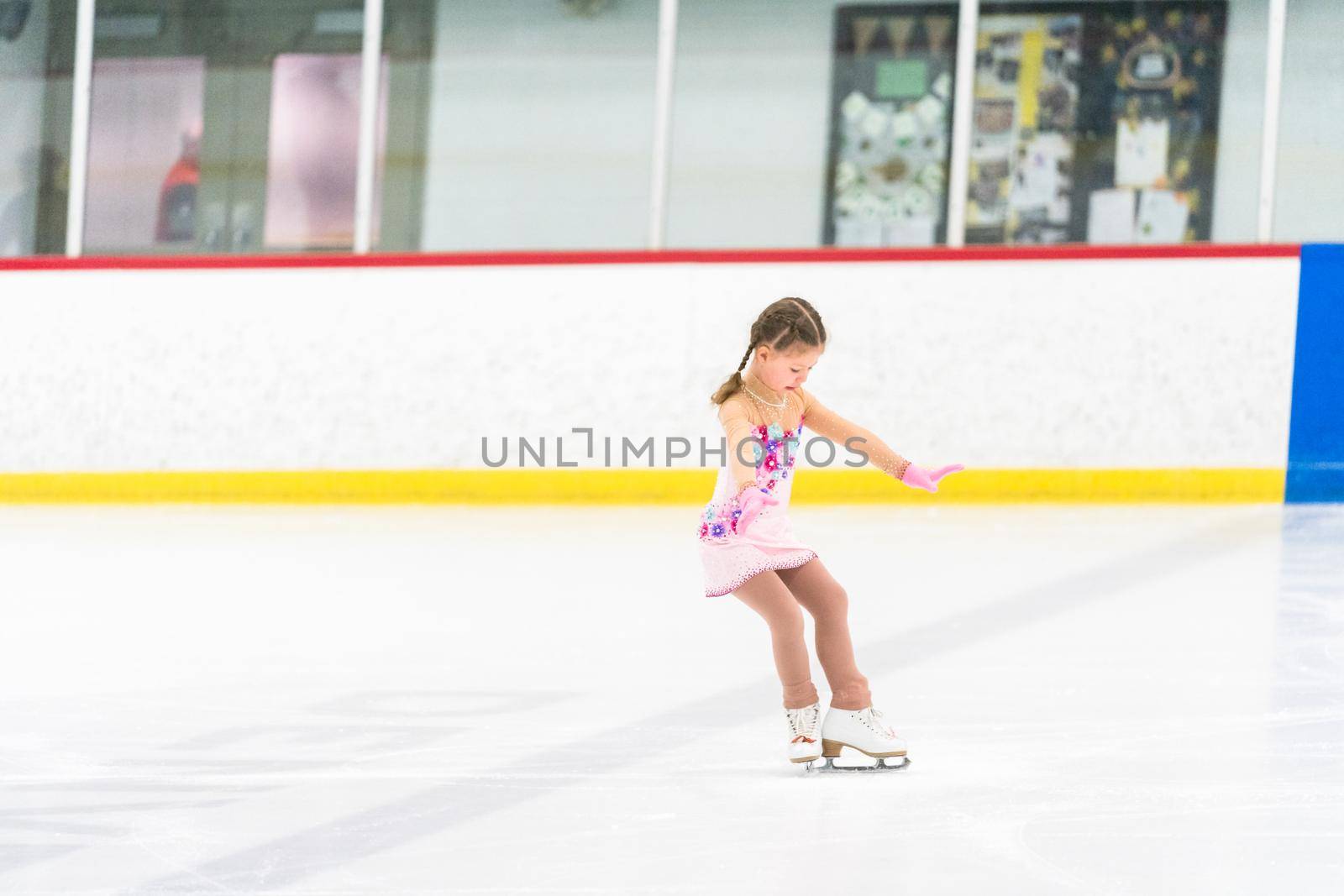 Little girl practicing figure skating on an indoor ice skating rink.