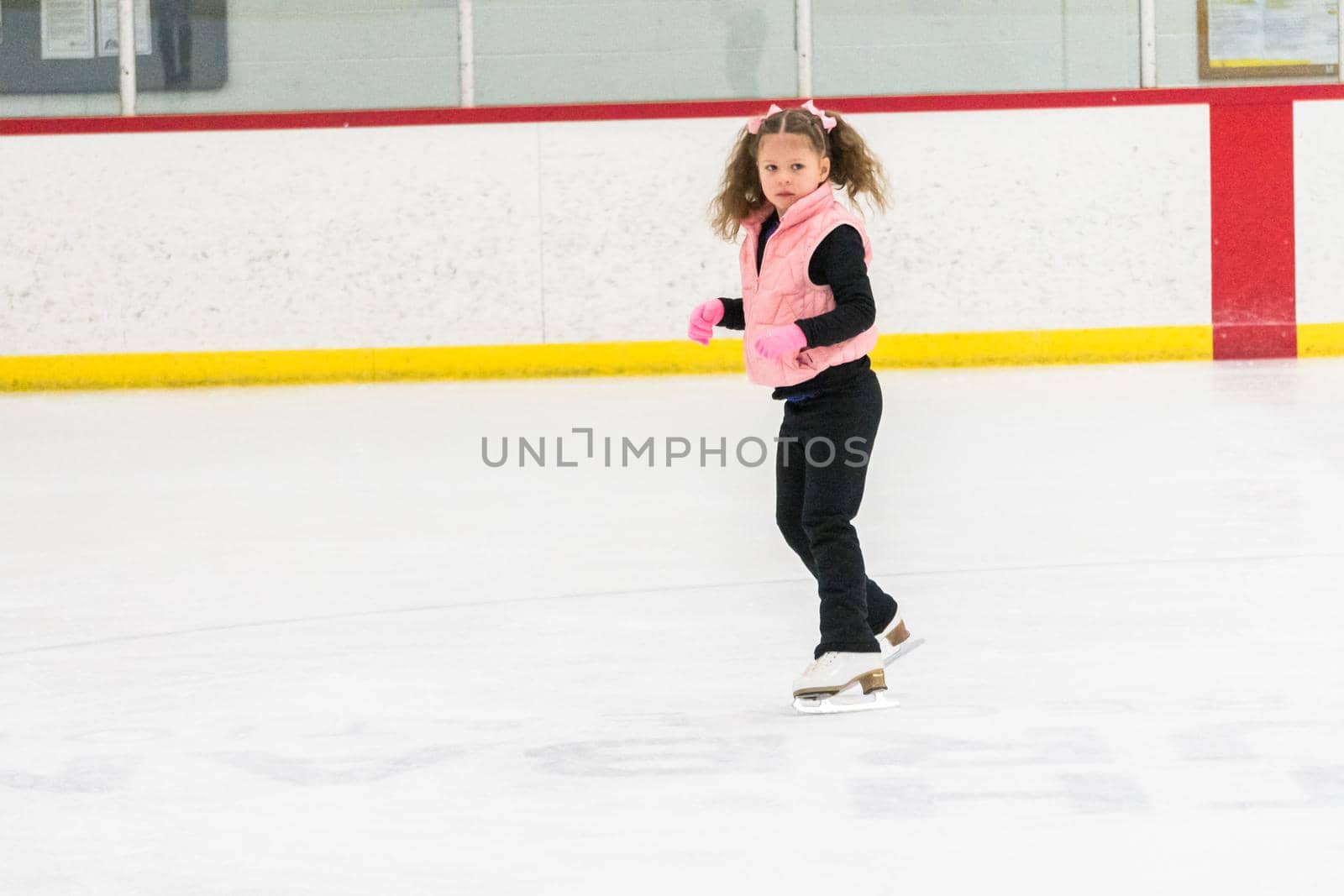 Little girl practicing figure skating moves on the indoor ice rink.