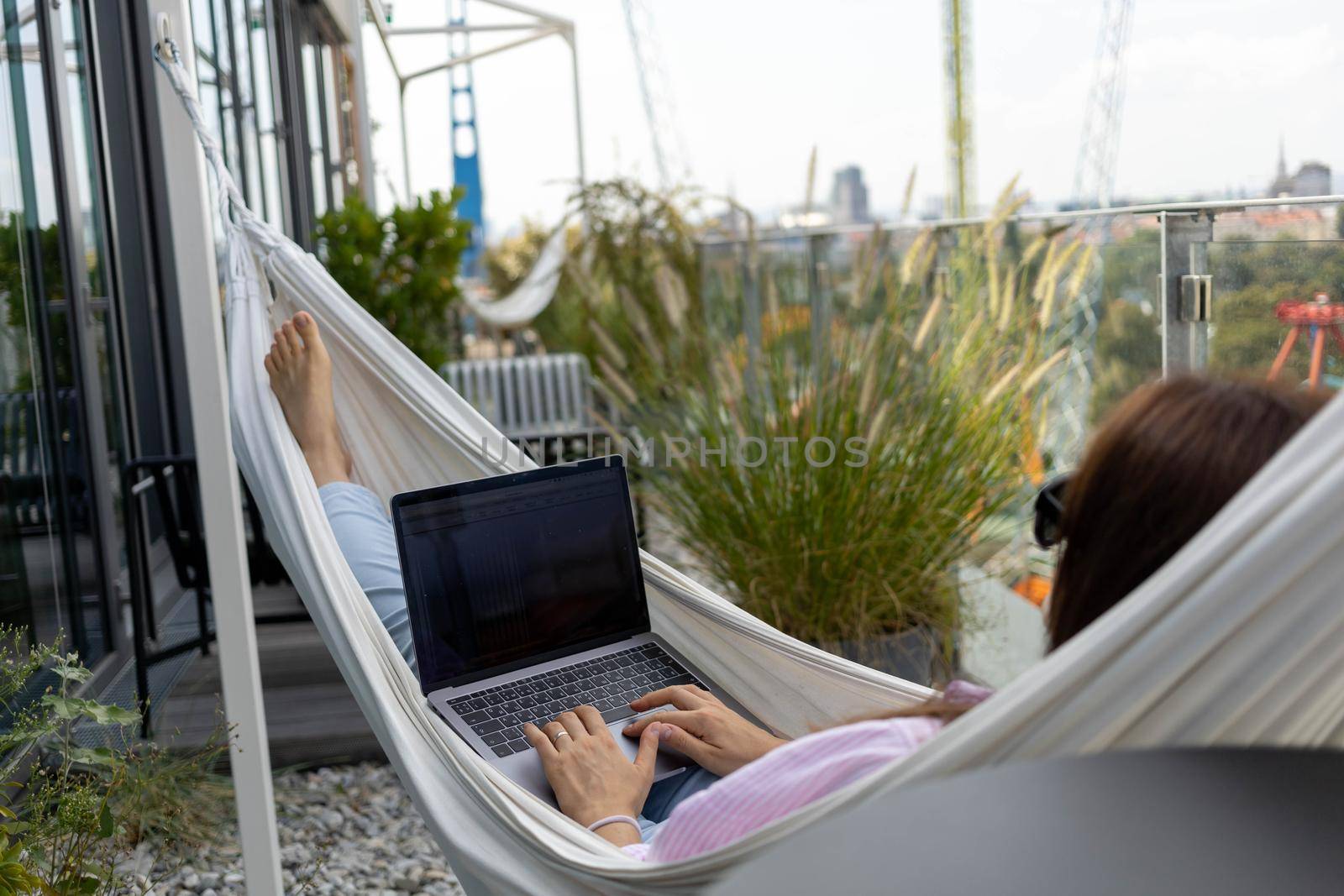 young woman freelancer working in hammock on terrace by Chechotkin