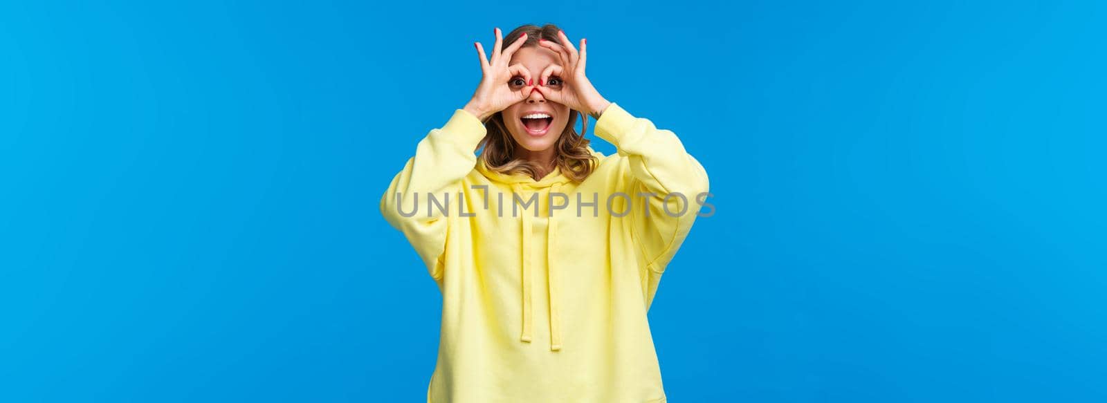 Carefree playful good-looking young blond woman playing around, make okay gesture or glasses with hands around eyes smiling joyfully, seeing something interesting on distance by Benzoix