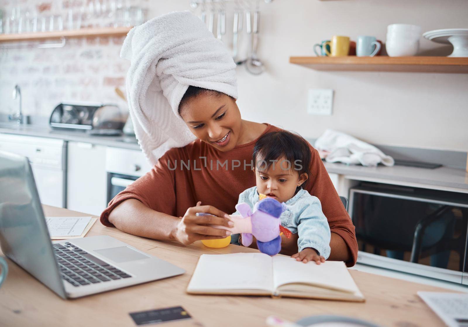Mother, baby and down syndrome with laptop for work on web, study or education in house. Multitasking, mom and child with computer, book and toys for learning, play and working while home in kitchen.