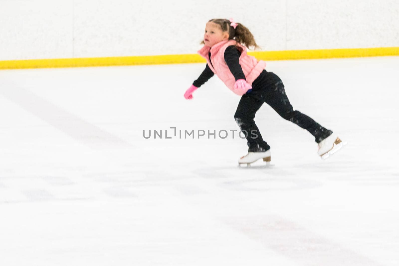 Little girl practicing figure skating moves on the indoor ice rink.