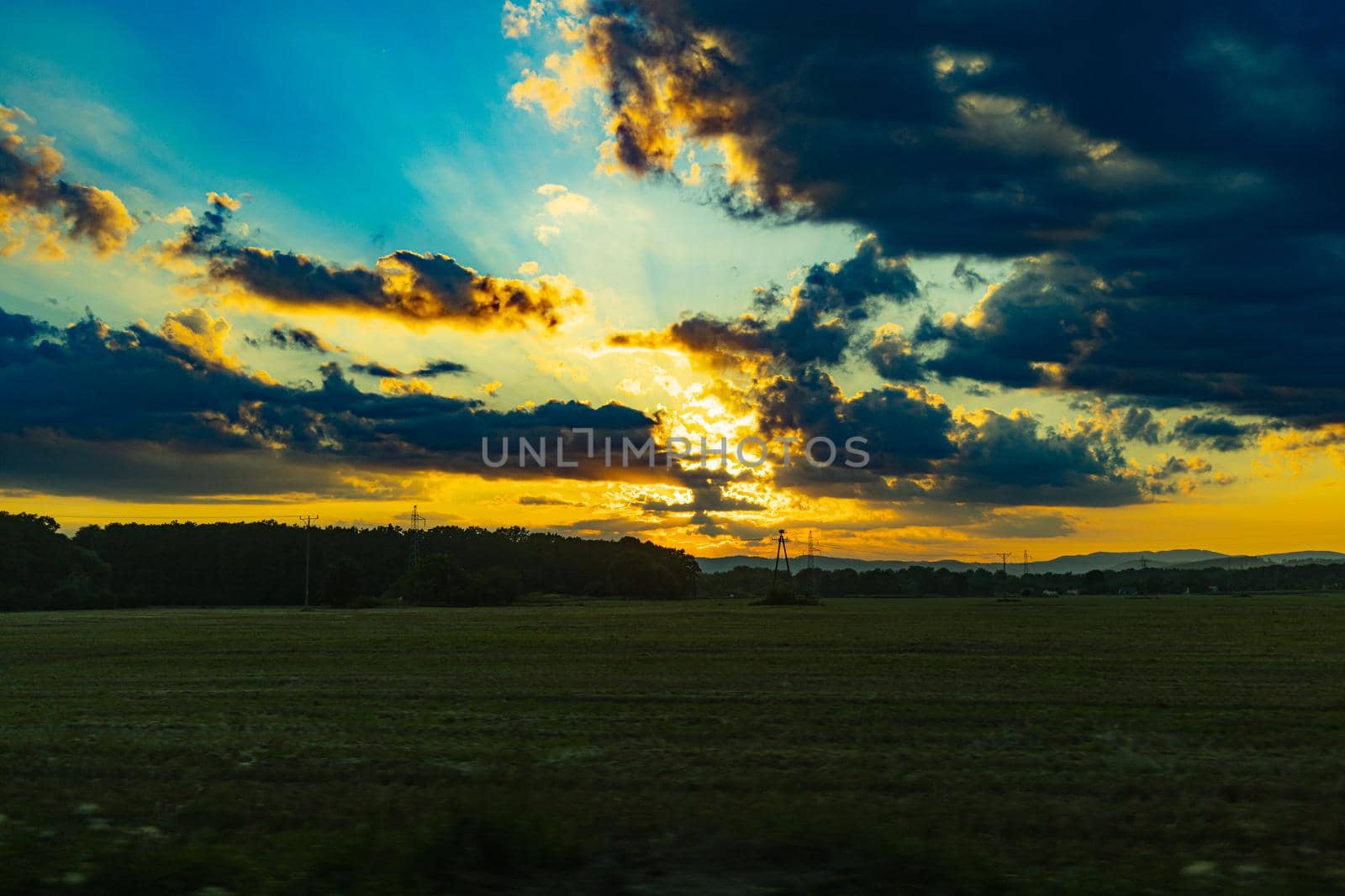 Beautiful shining sun behind big clouds at sunset over big fields