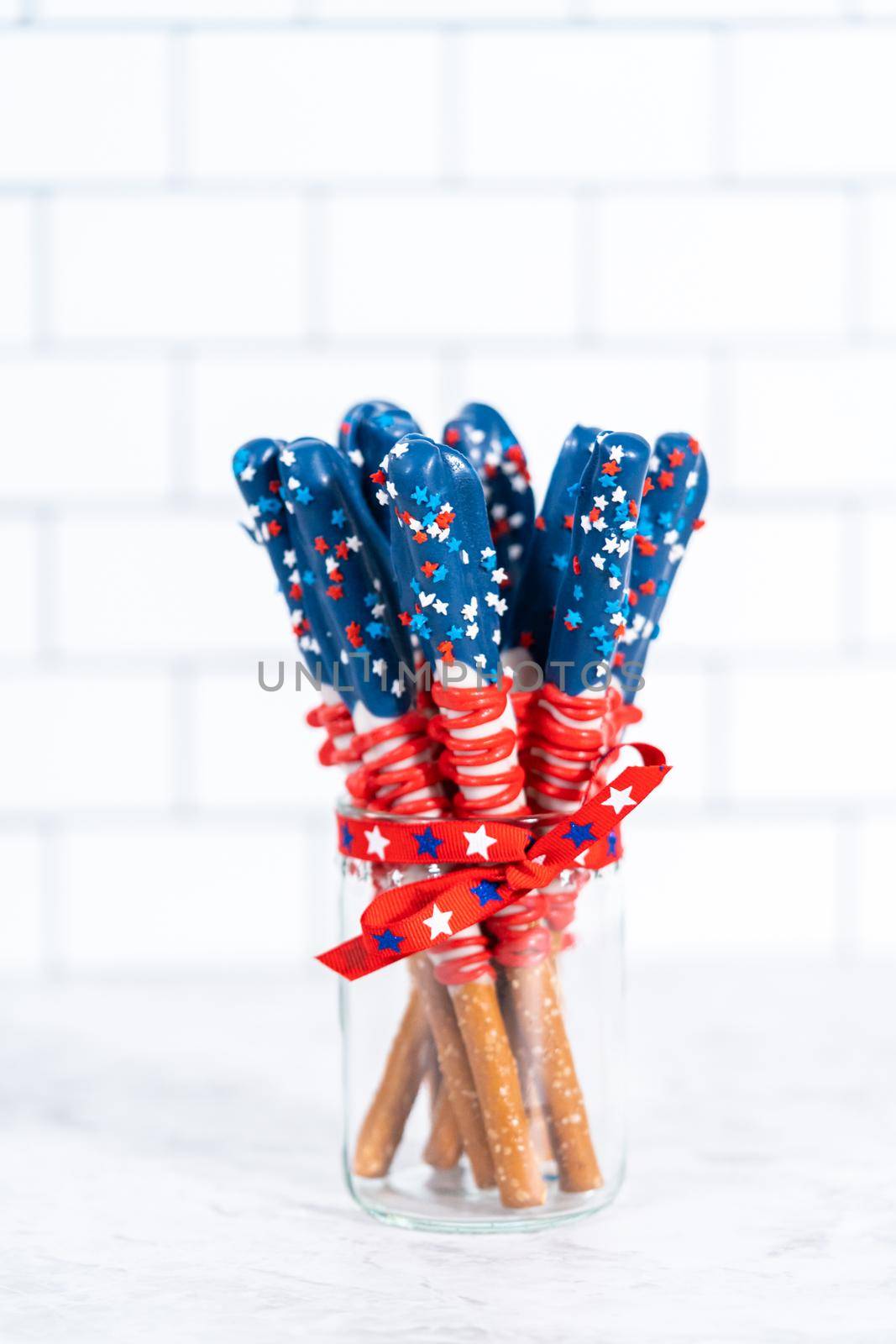 Homemade chocolate-covered pretzel rods decorated like the American flag in a glass jar.