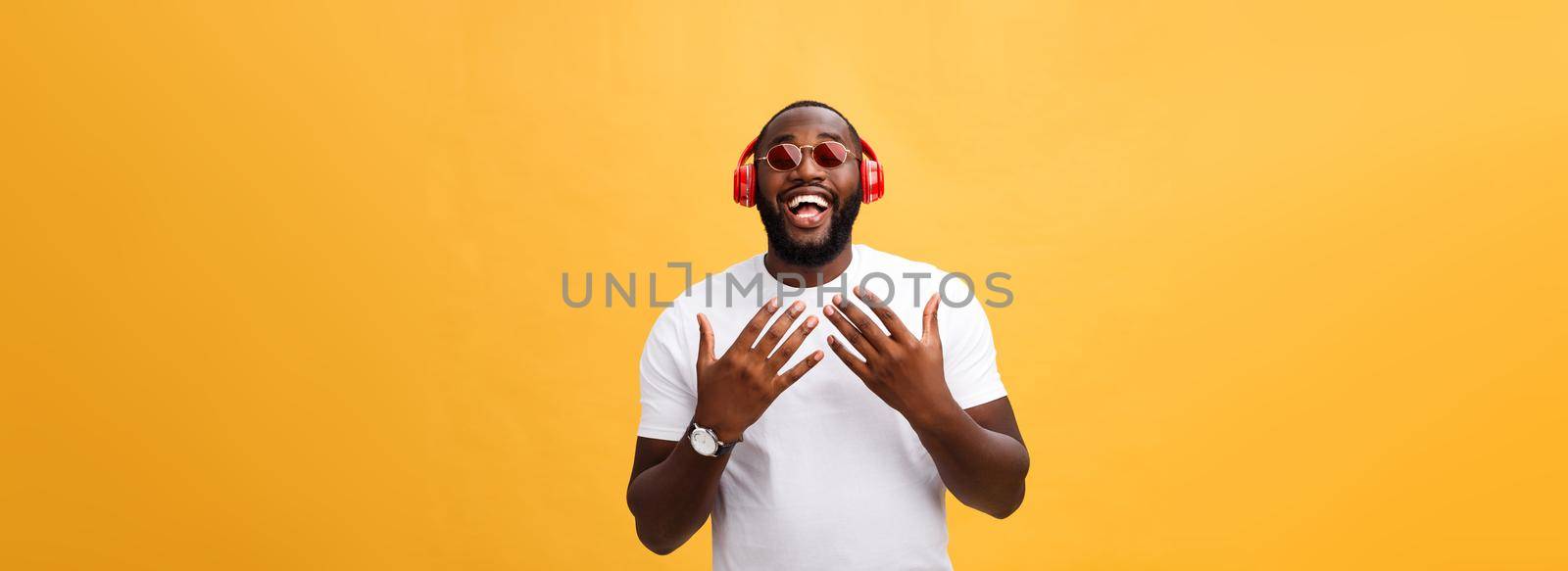 Handsome young African American man listening and smiling with music on his mobile device. Isolated over yellow background. by Benzoix