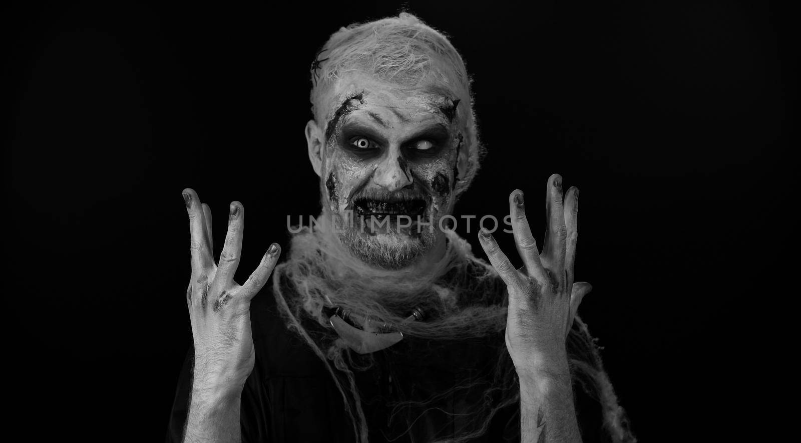 Sinister man horrible scary Halloween zombie listening music dancing disco fooling around having fun expressive gesticulating hands. Dead guy alone with wounded bloody scars face on black background