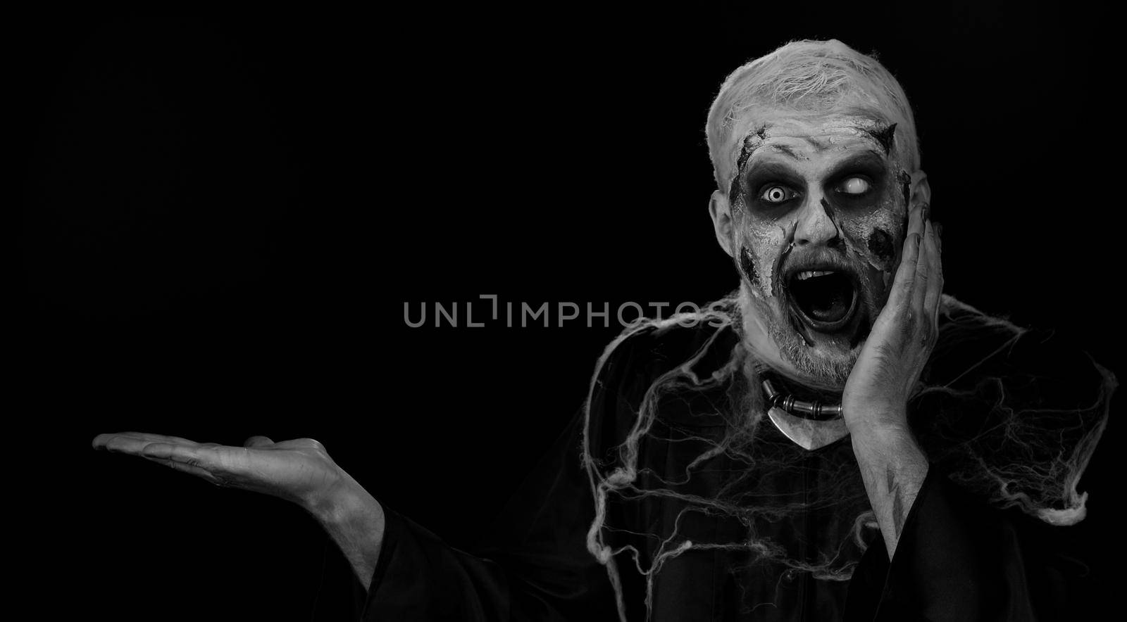 Wow surprise. Zombie man with fake wounds scars make-up showing thumbs up and pointing empty place, advertising area for commercial text logo, copy-space for goods promotion. Halloween ugly dead guy