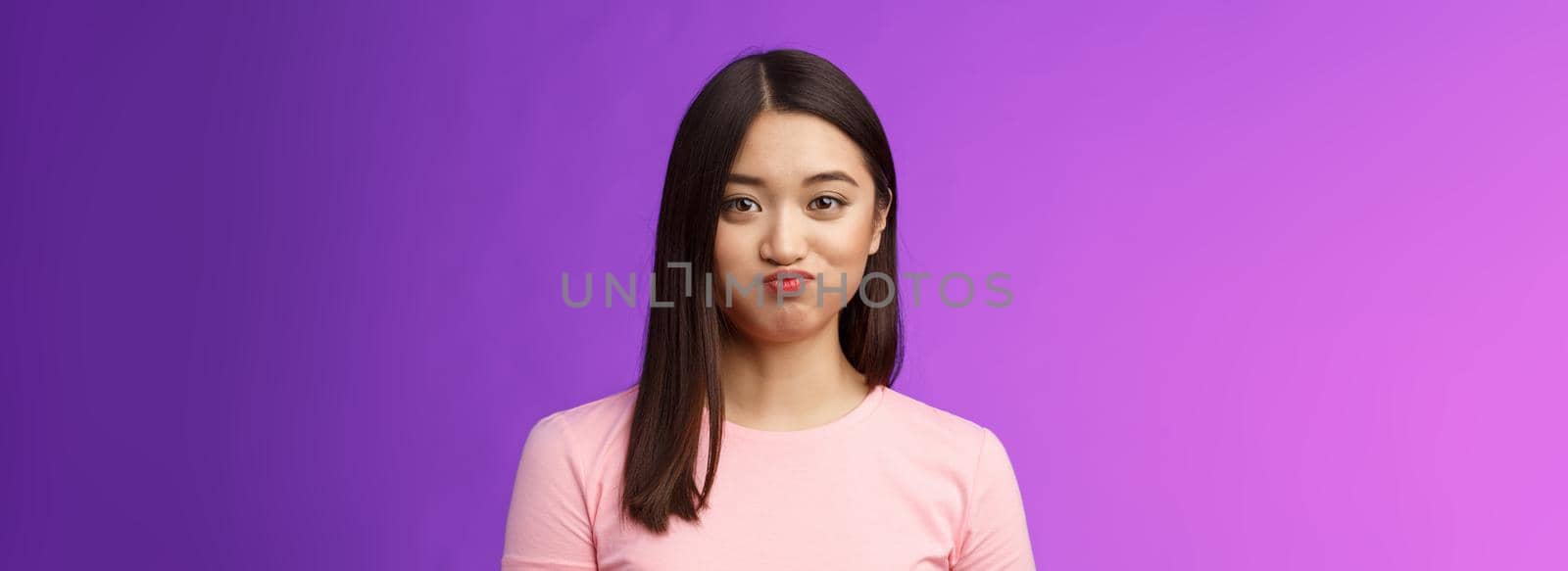 Close-up cute tender young asian female holding breath speechless, smiling silly having challenge hiding secret unwilling talk, pouting lovely, look camera entertained, purple background.