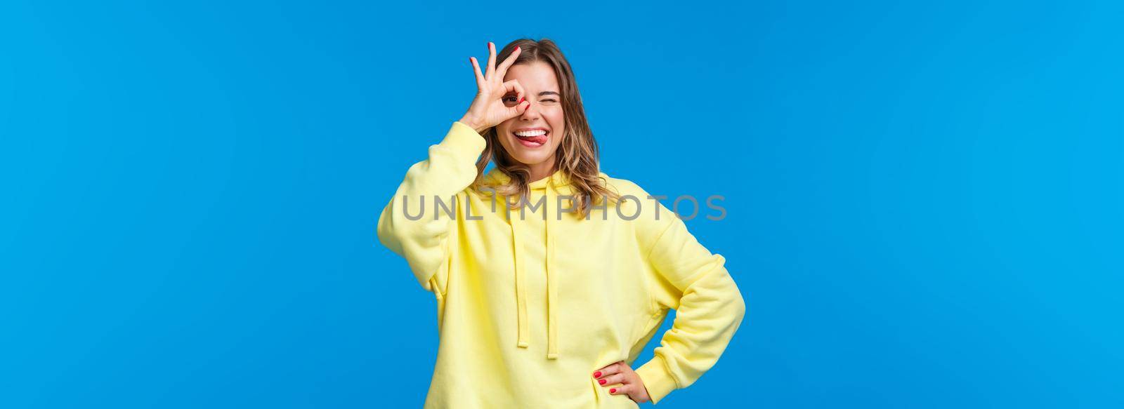 No problem, stay relaxed. Carefree and chill good-looking blond girl vibing, assure all okay nothing worry about, show tongue wink and look through okay gesture, blue background.