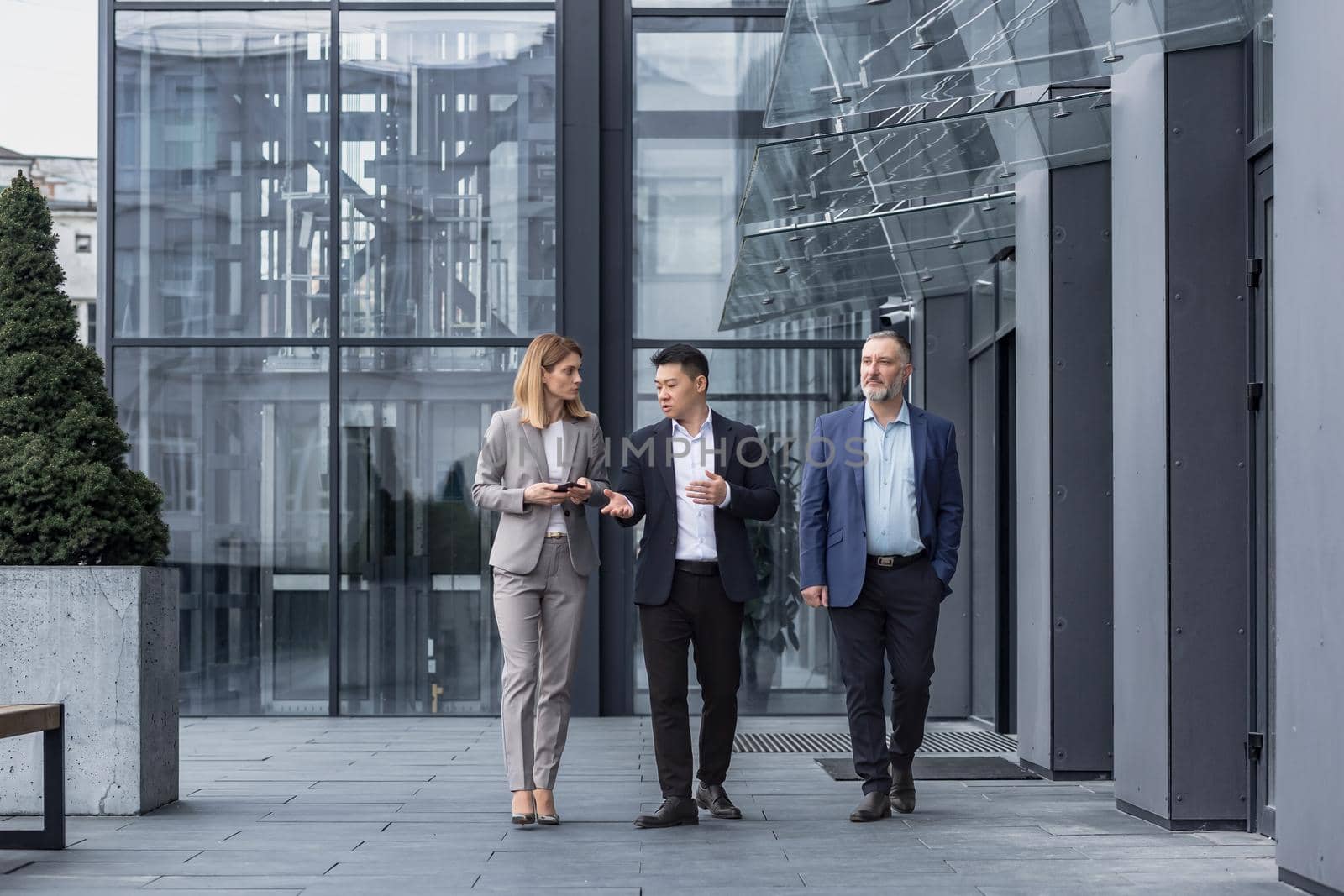 Three diverse business people walking and talking focused and thoughtful seriously outside office building, male and female, discussing plans and work project