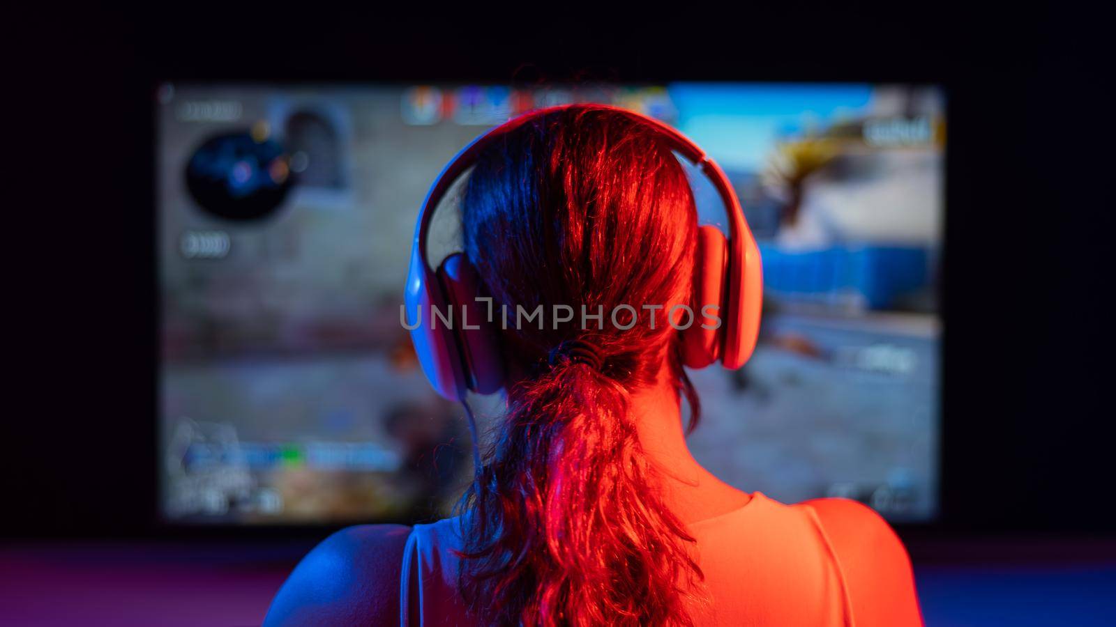 Rear view of a caucasian woman playing a computer game in neon light in the dark. by mrwed54