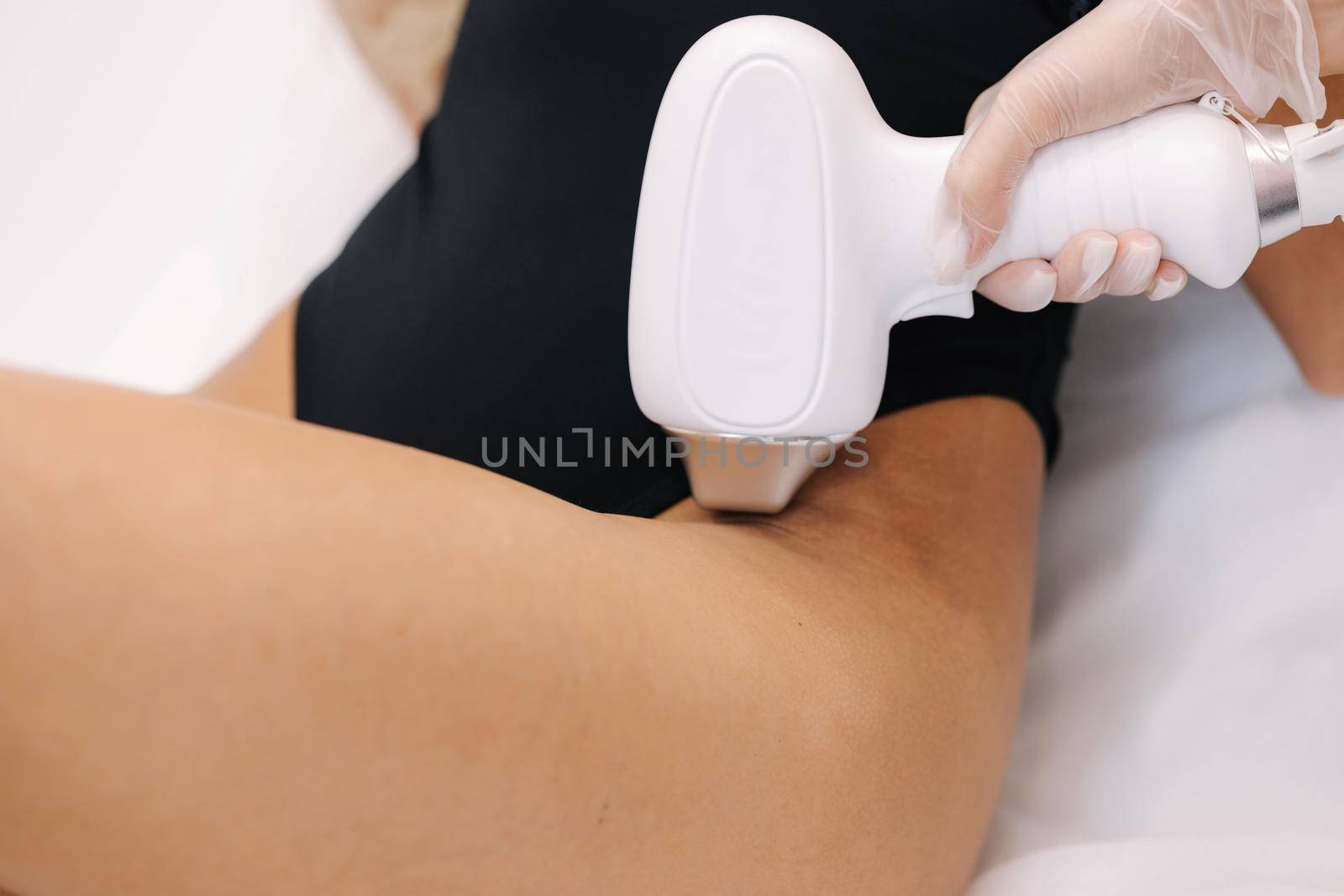 Cosmetology. Beautiful woman receiving laser hair removal procedure at beauty salon. Beautician doing beauty treatment for female arm at spa salon. Protective glasses. Close-up of bikini area.