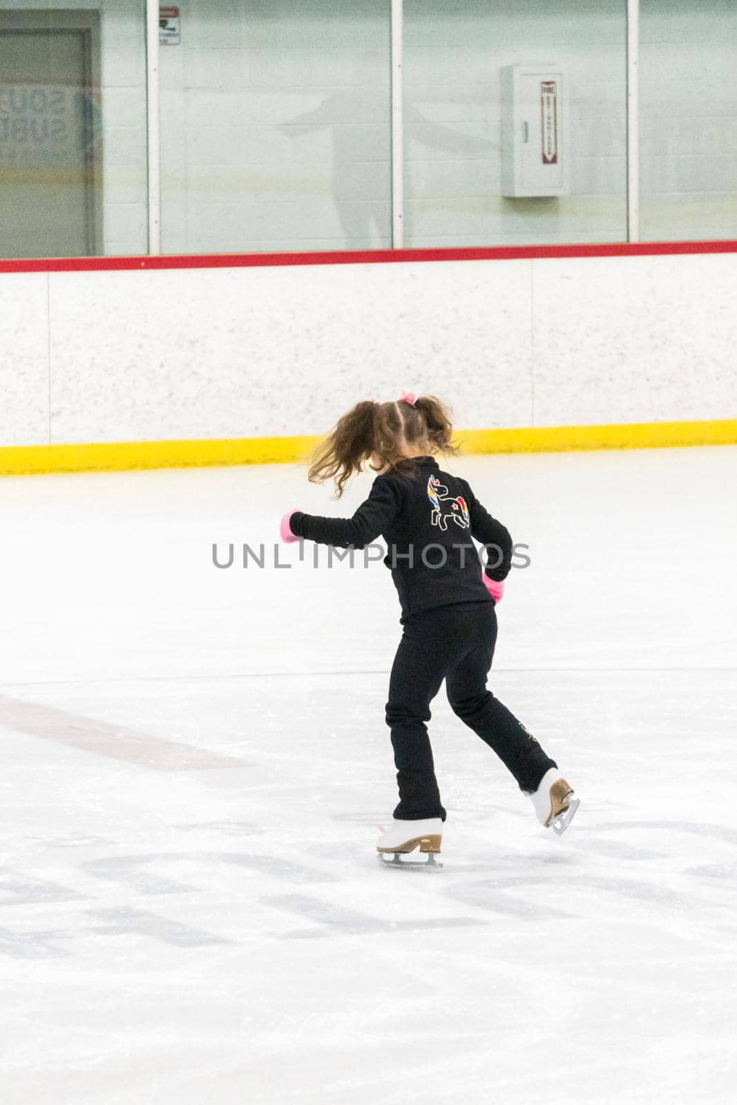 Little girl practicing figure skating moves on the indoor ice rink.