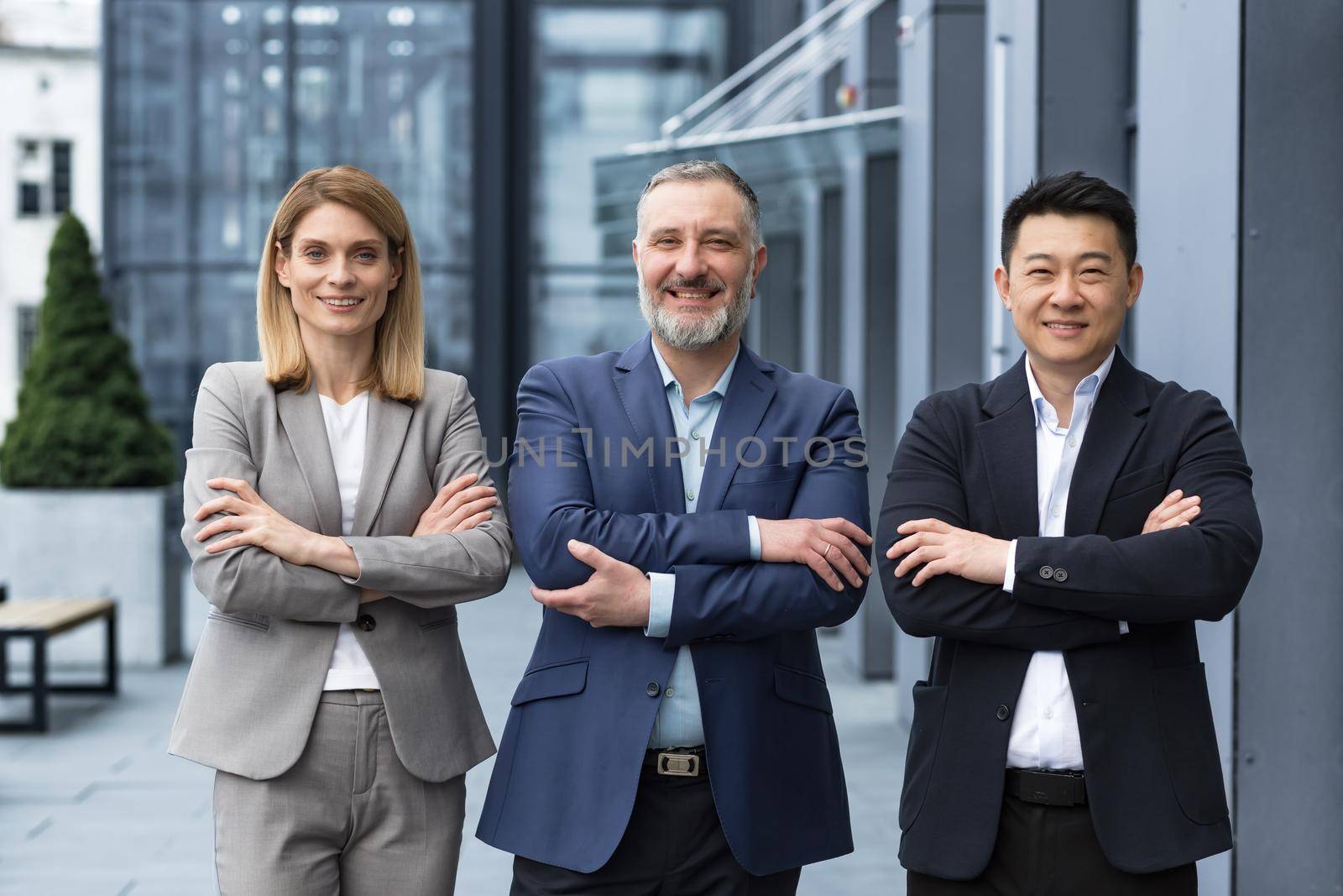 Successful dream team, diverse business group of asian man and business woman smiling and looking at camera, colleagues with crossed arms outside office building, professionals investors and bankers