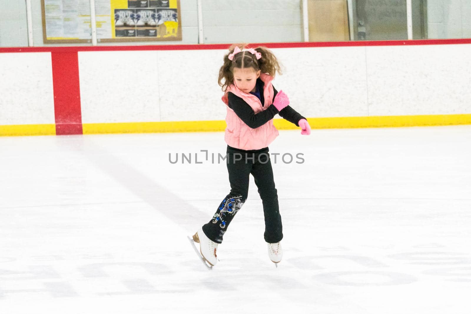 Little girl practicing figure skating moves on the indoor ice rink.