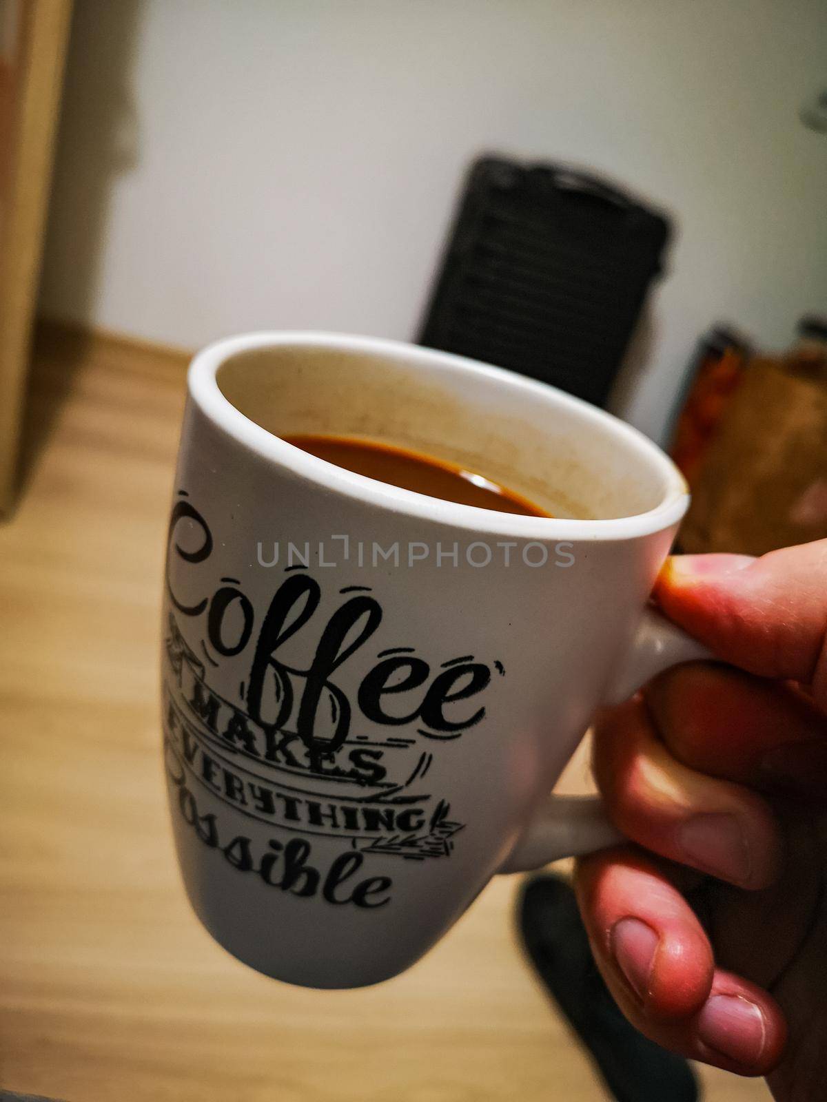 White cup full of letterings of coffee keeped in hand inside room by Wierzchu