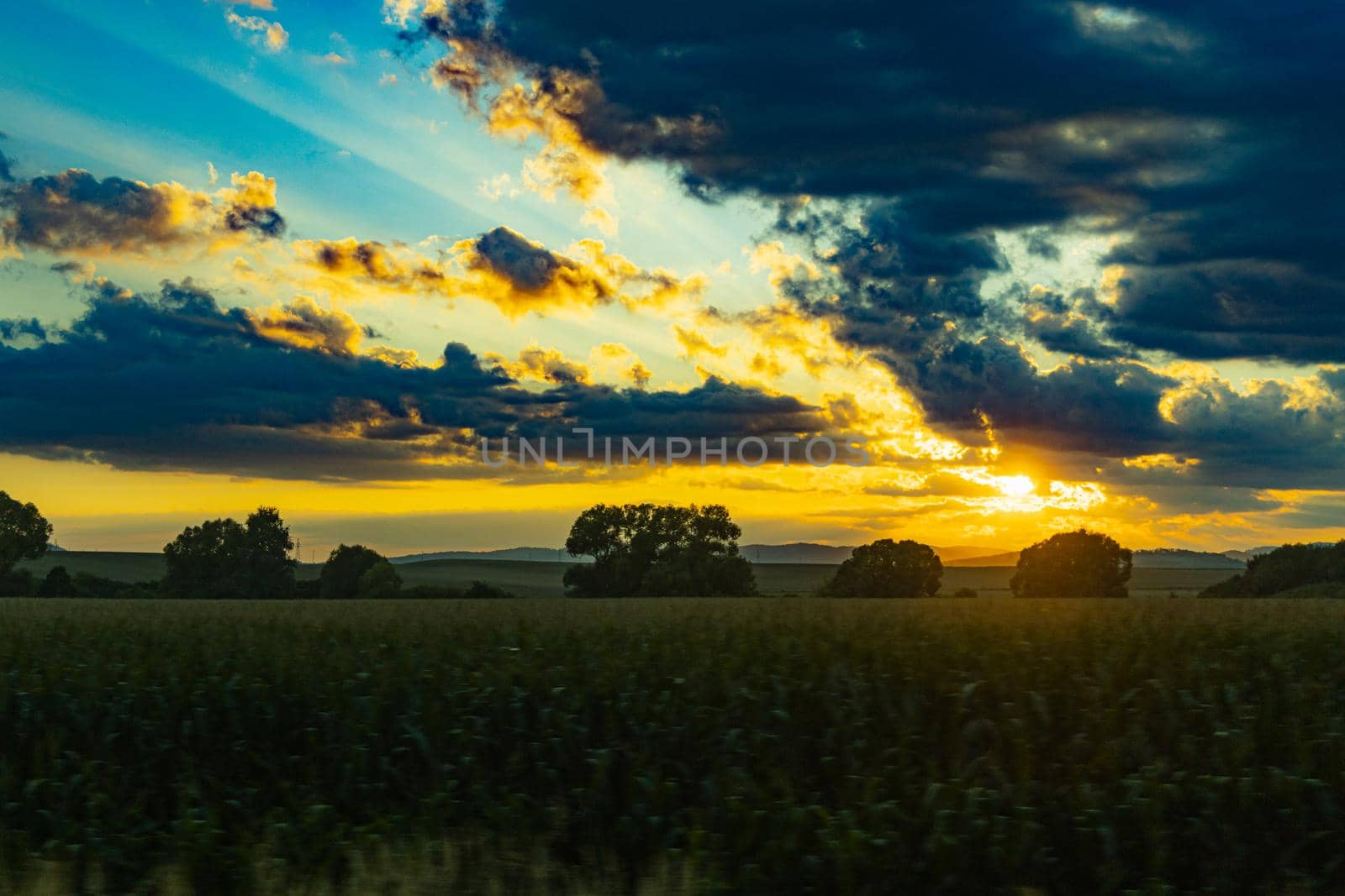 Beautiful shining sun behind big clouds at sunset over big fields by Wierzchu