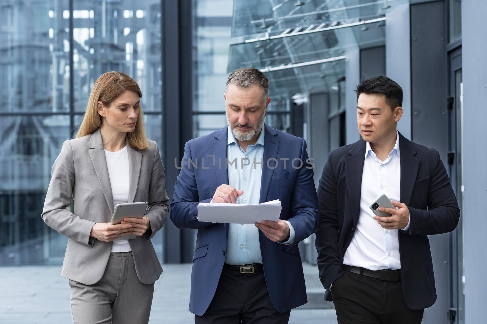 Diverse business team three colleagues employees discuss documents contract outside office building businessman and businesswoman holding bills and financial reports talking
