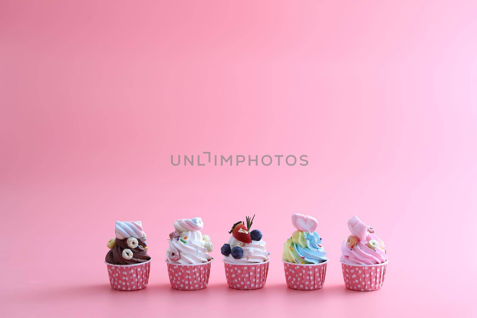 Colorful cupcakes isolated in pink background by piyato