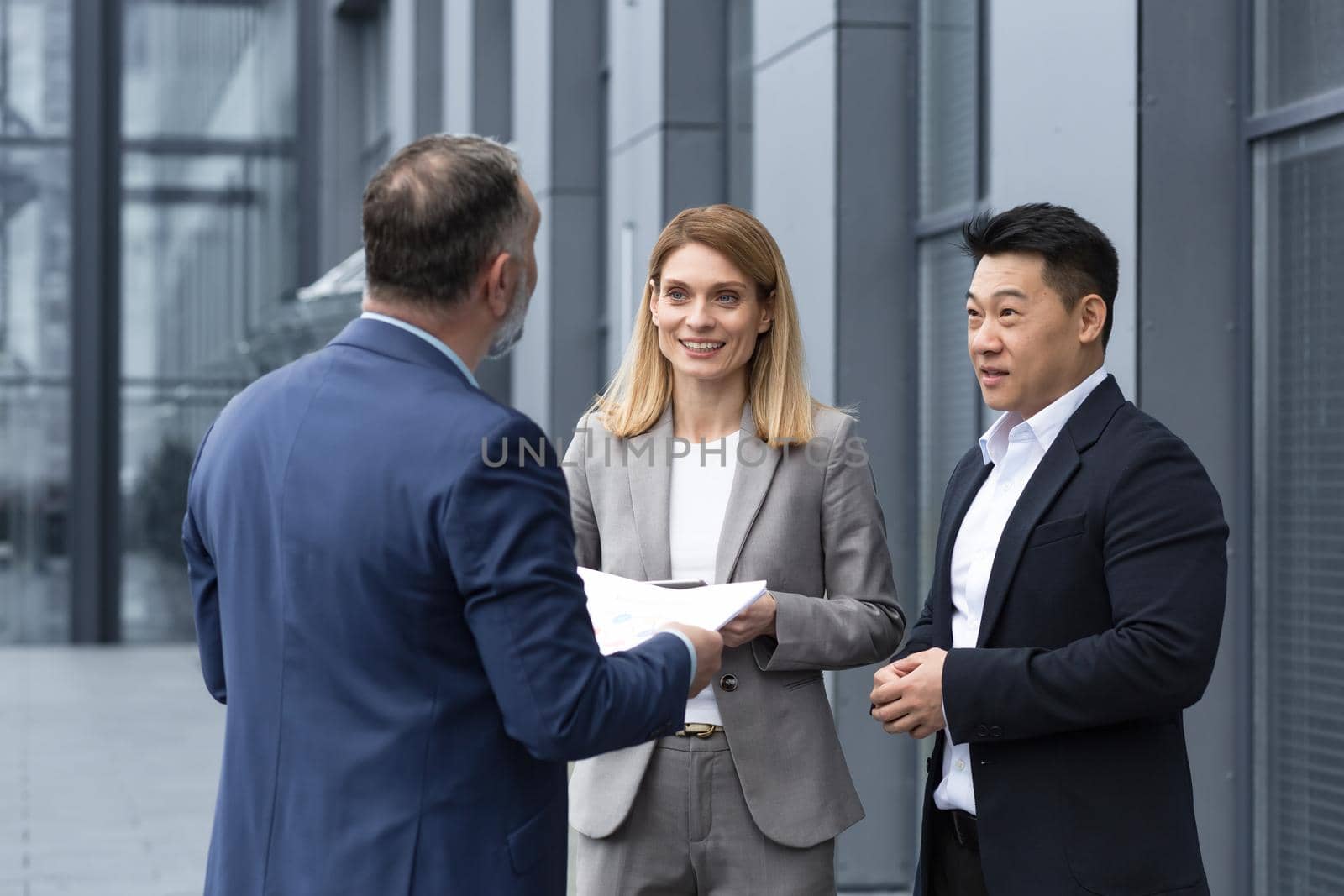International business team meeting mature man, Caucasian woman, Asian employee communicate . group of entrepreneurs in formal suits discuss a project document near office center on street