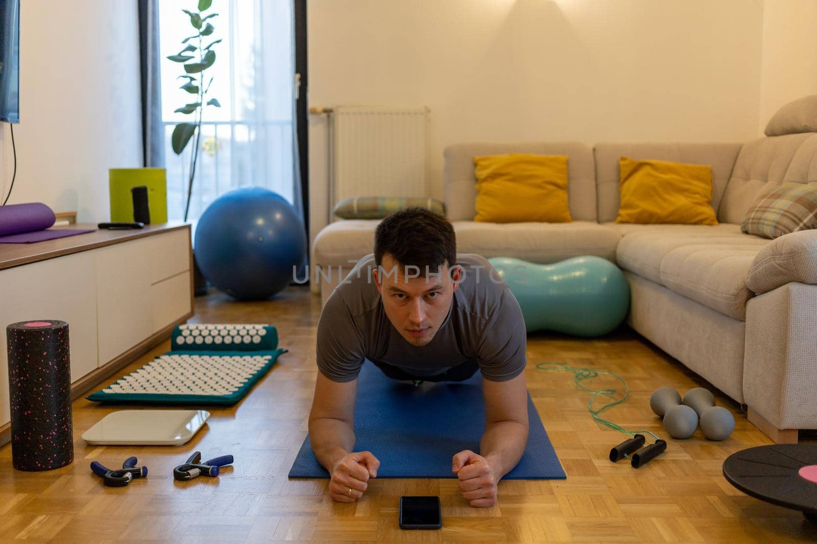 young man exercising doing workout at home in front of smartphone by Chechotkin