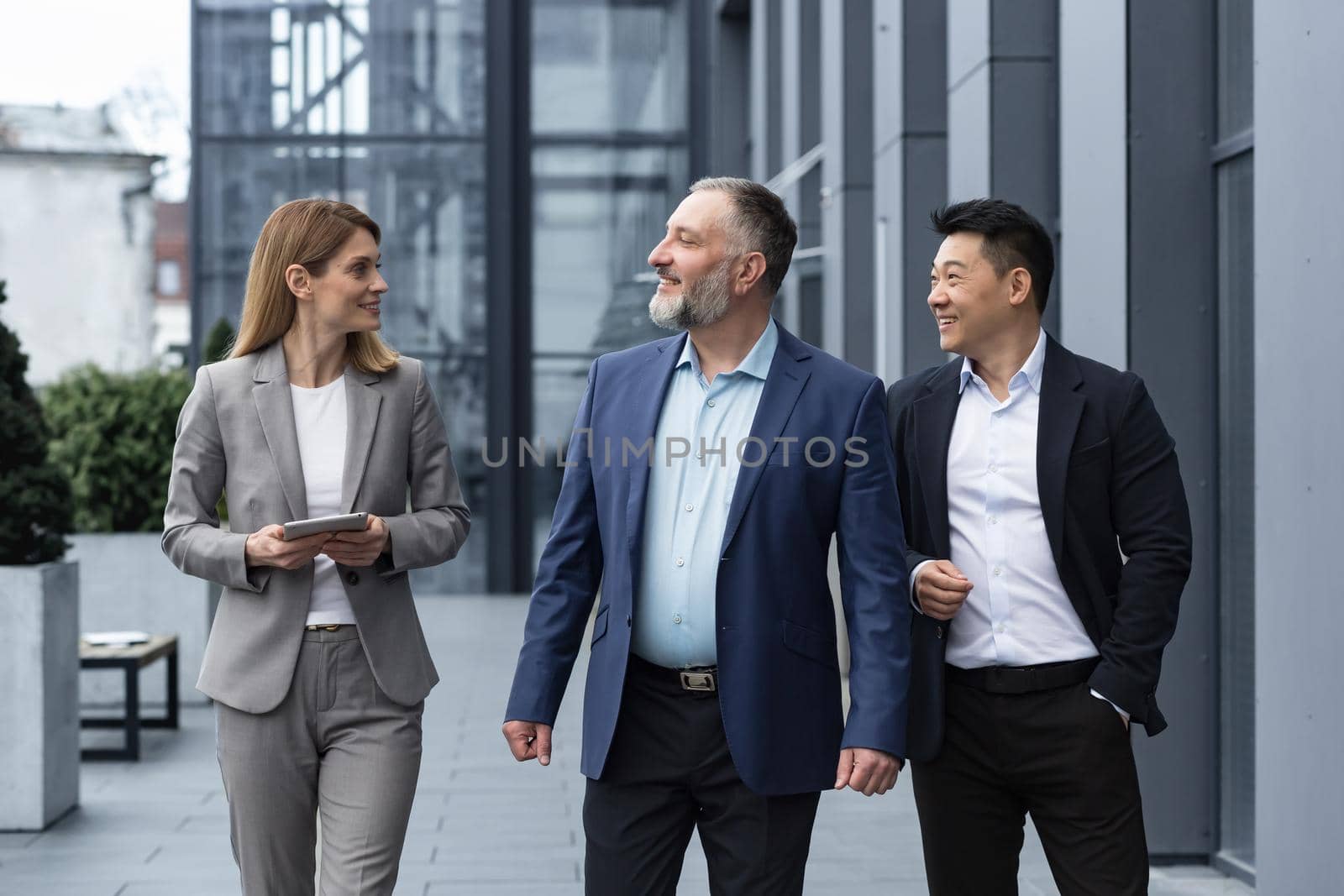 A diverse team of IT specialists, senior and experienced engineers managers team leaders, a group of three workers happily strolling outside an office building, colleagues in business suits by voronaman