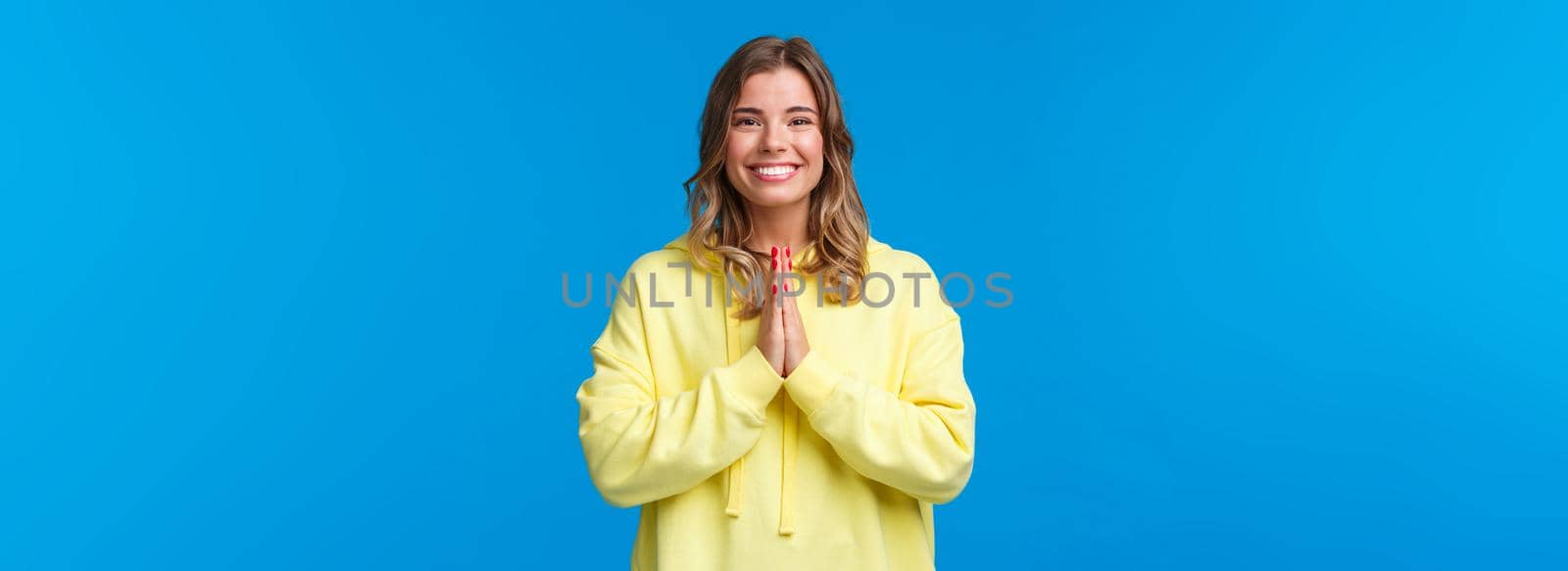 Cheerful young european female practice yoga, greeting sensei with namaste gesture, hold hands in pray and smiling grateful with relaxed carefree expression, smiling camera, blue background.