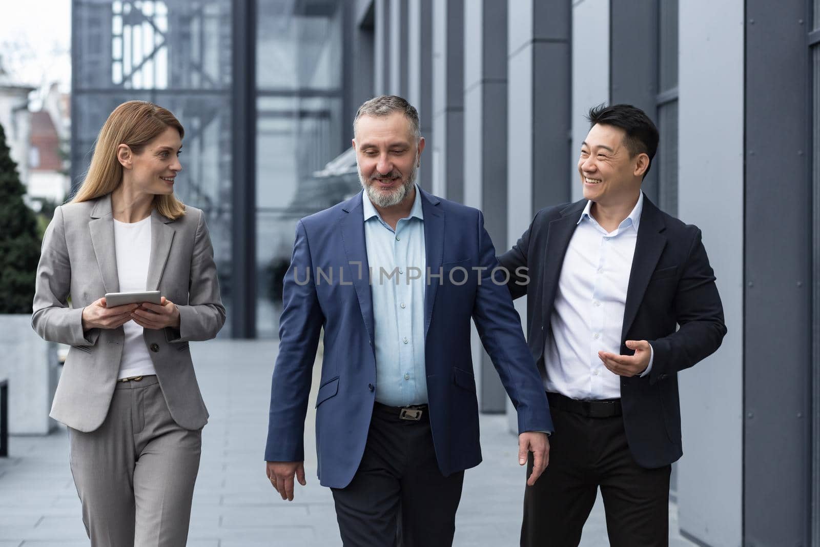 A diverse team of IT specialists, senior and experienced engineers managers team leaders, a group of three workers happily strolling outside an office building, colleagues in business suits by voronaman