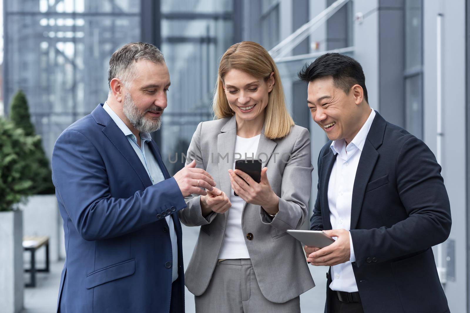 Three colleagues employees watch funny videos or look at photos, pictures memories looking at smartphone screen using mobile phone. group of business people office workers having fun on breaks