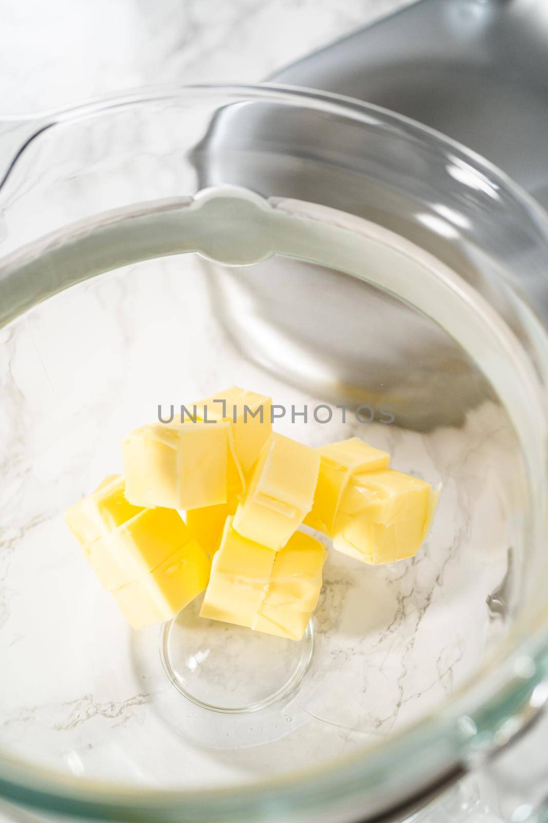 Mixing ingredients in a large glass mixing bowl of kitchen mixer to make eggnog buttercream frosting.