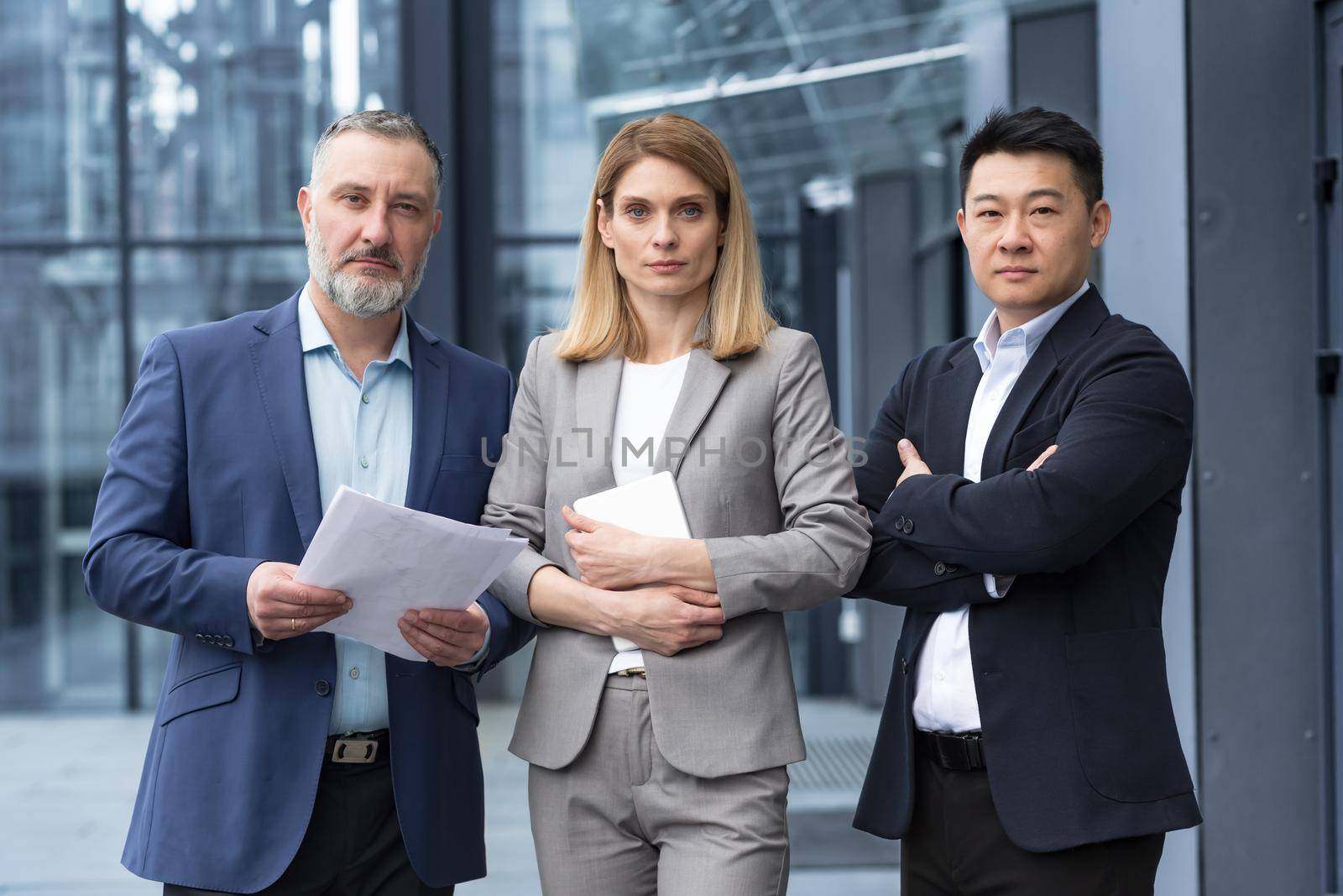 A team of experienced team leaders and specialists, a diverse group of business people, three people in business clothes are serious and focused in business clothes looking at the camera